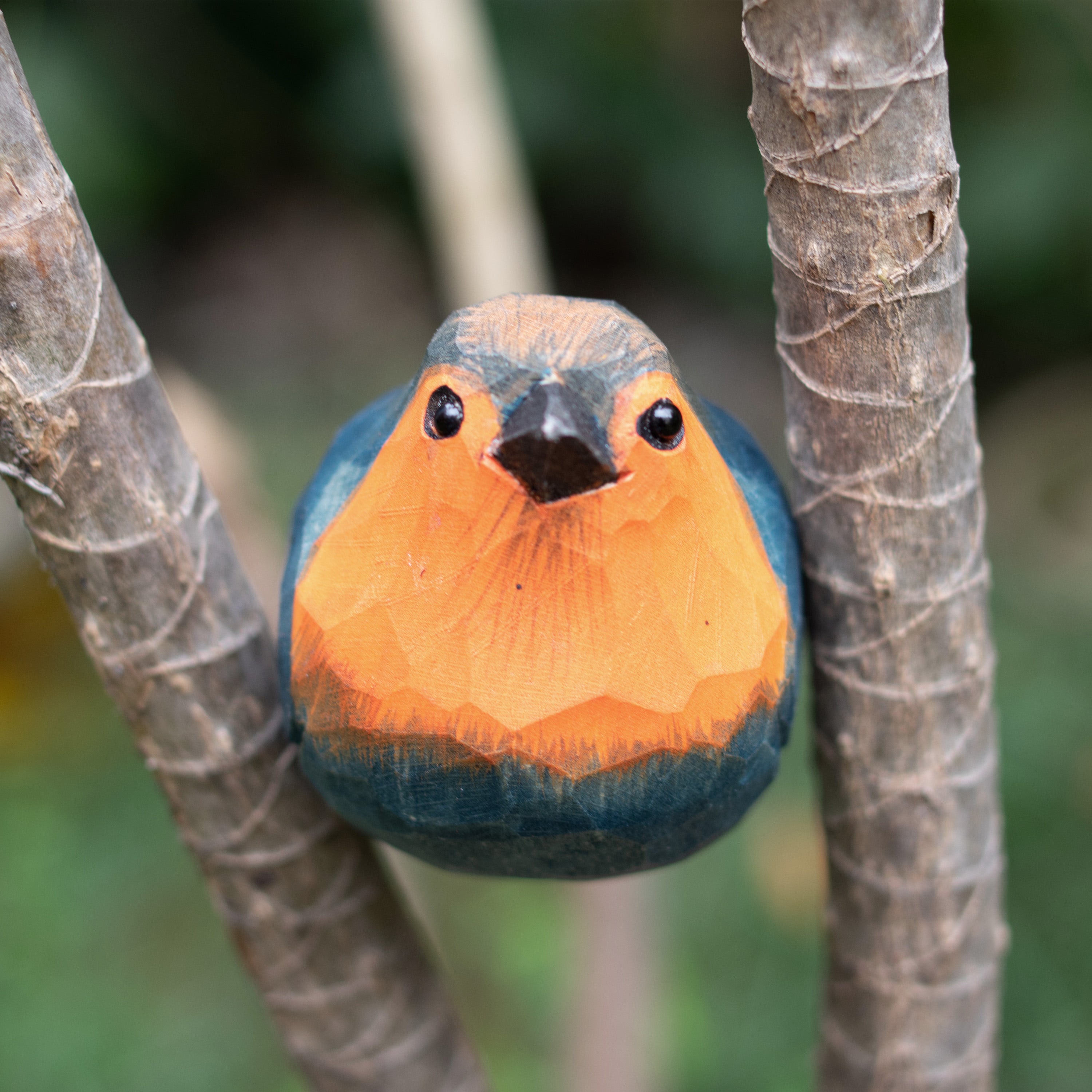 Hand-carved wooden figurine of a European Robin perched on a branch, with a predominantly red and blue color palette.