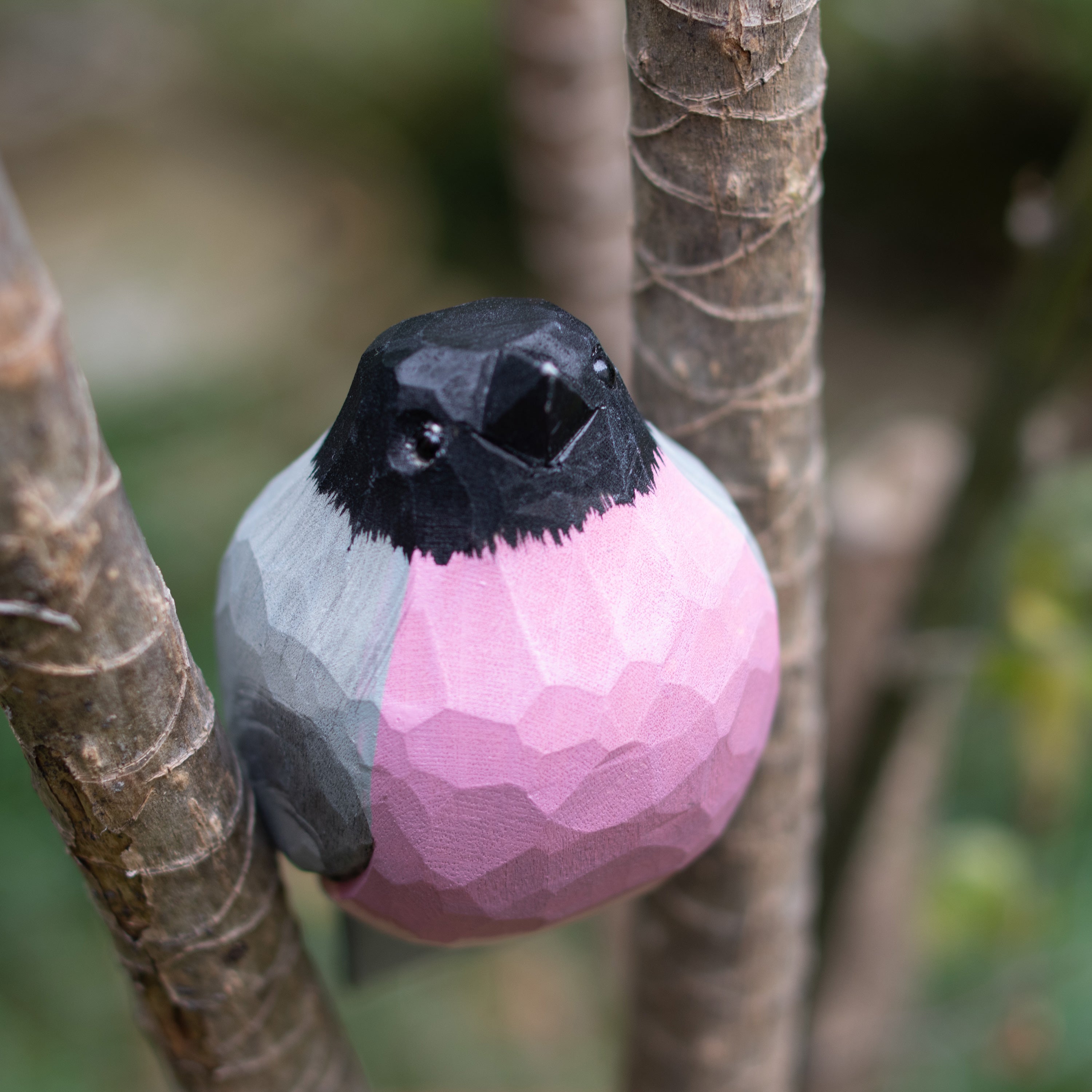A hand-carved wooden figurine of a Bullfinch perched on a branch.