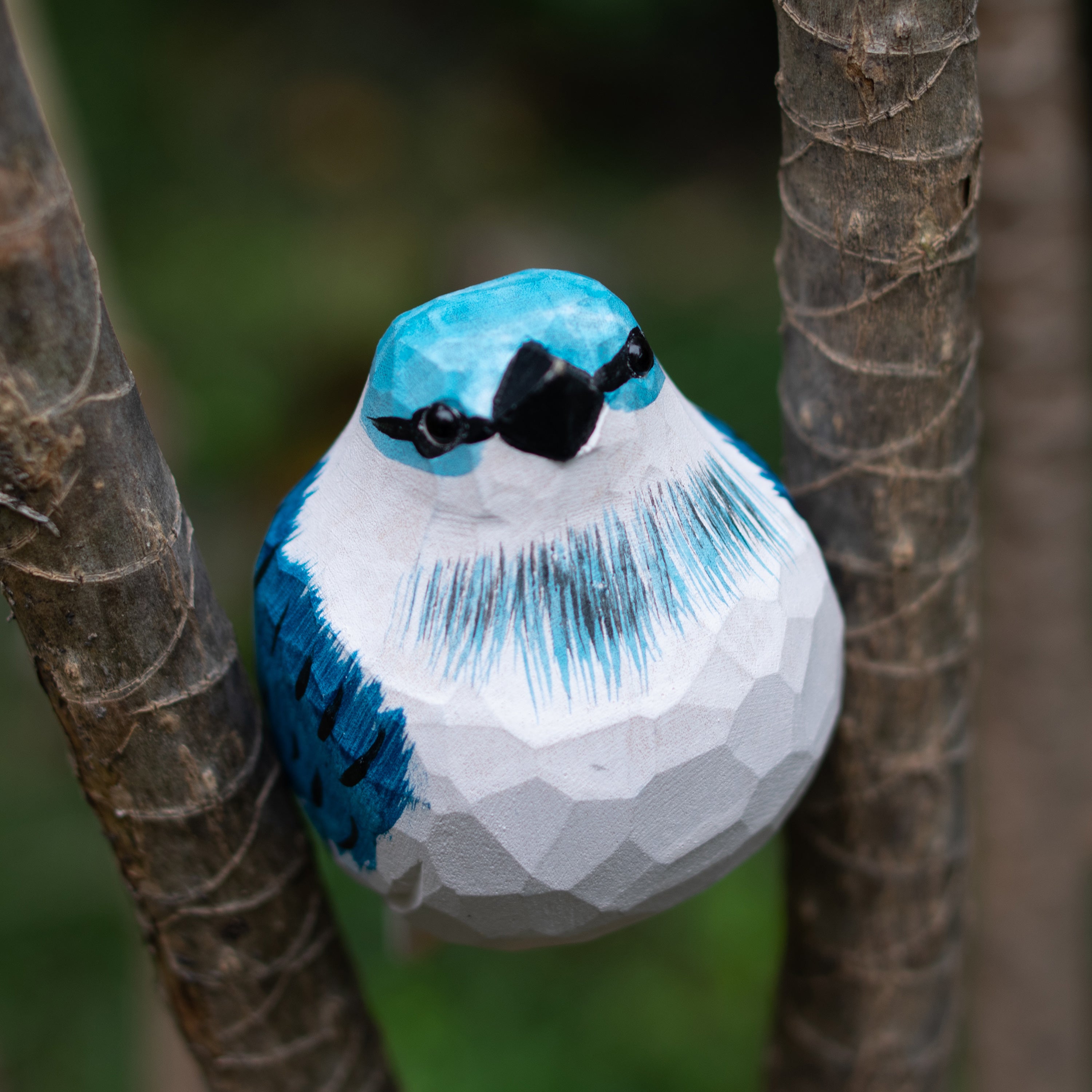 A hand-carved wooden figurine of an Azure Tit perched on a branch, with vibrant blue and white plumage.