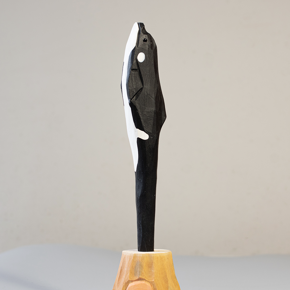 Handcrafted wooden orca penon a wooden base against a plain background