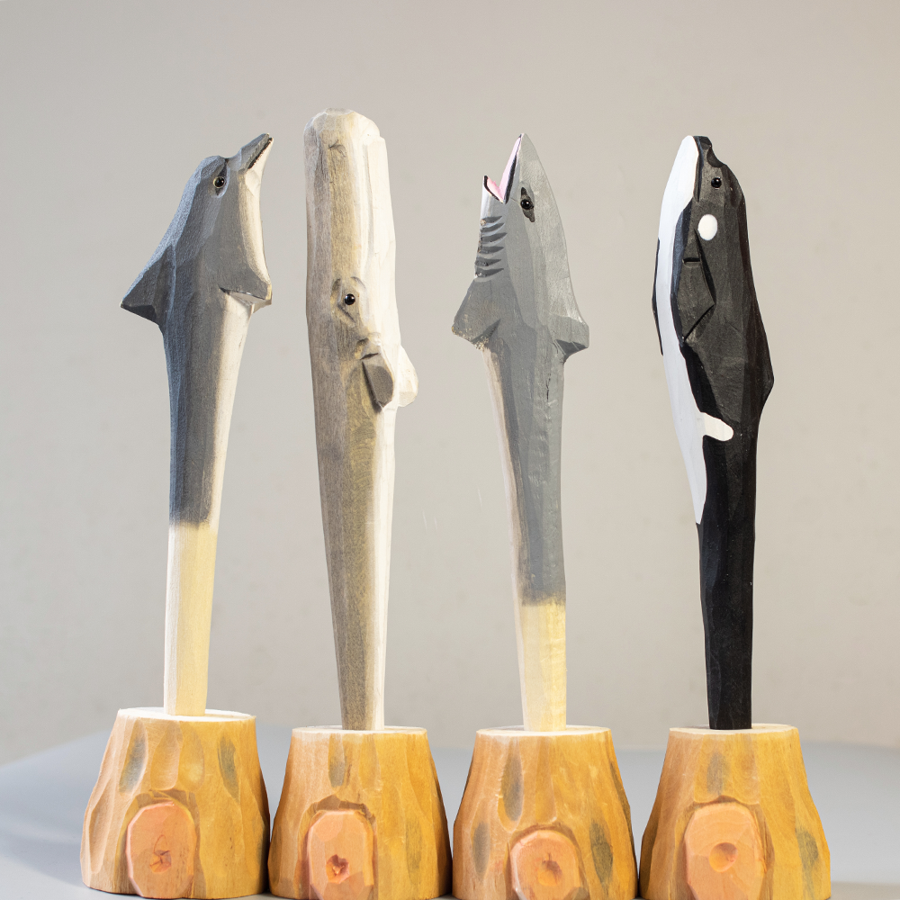 Four wooden pen shaped like animals on stands against a plain background