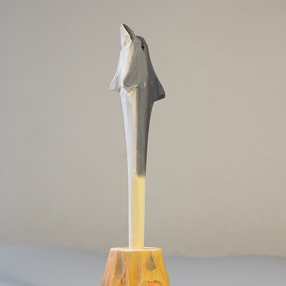 Metallic shark pen on a wooden base against a neutral background