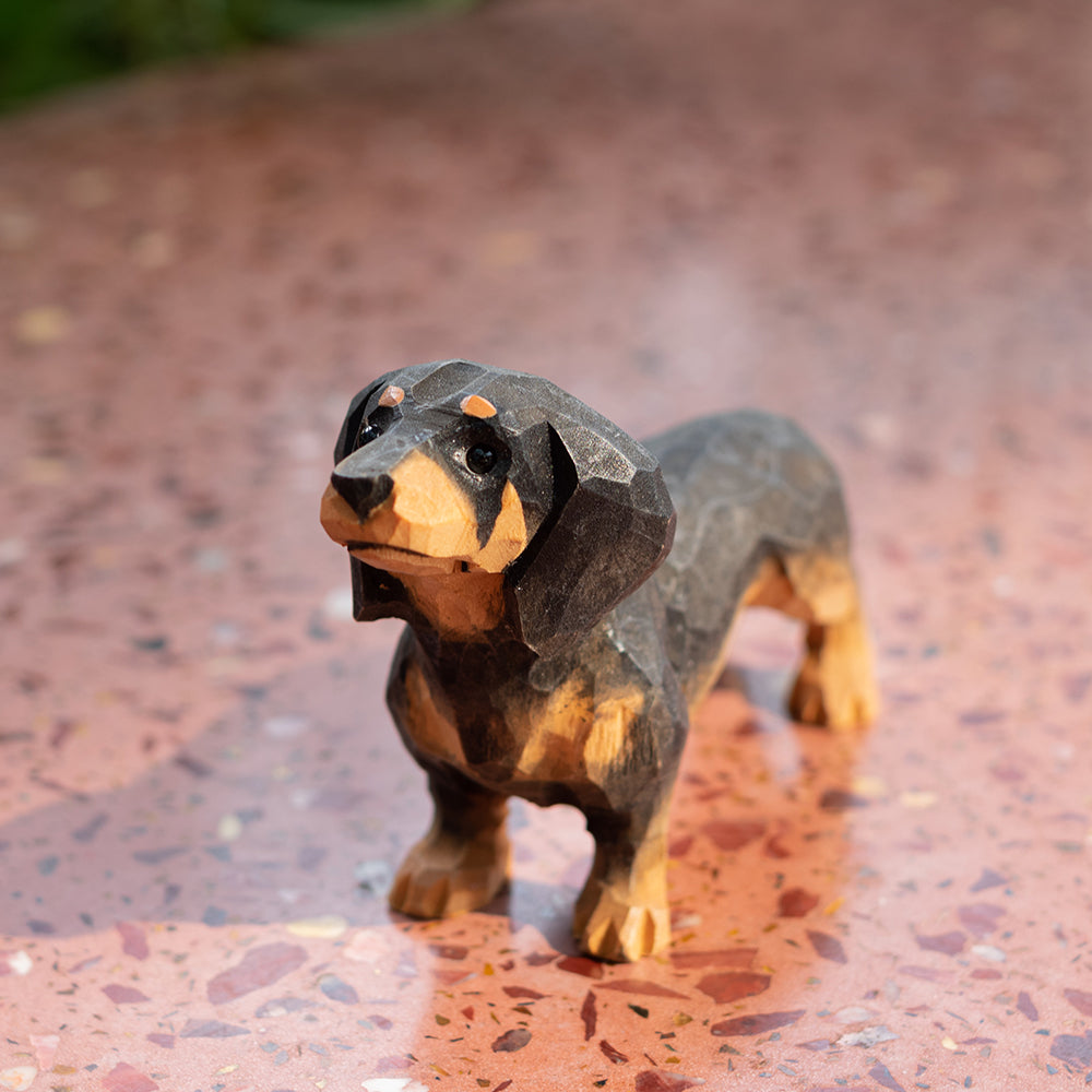 A hand-carved basswood figurine of a black dachshund dog, placed on a textured surface.