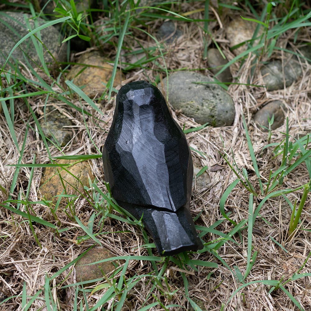 Wooden blackbird figurine with a red beak on grass and rocks