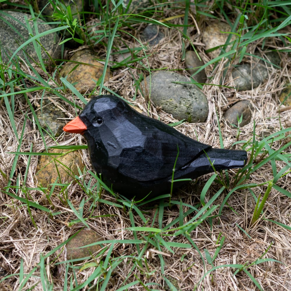 Wooden blackbird figurine with a red beak on grass and rocks