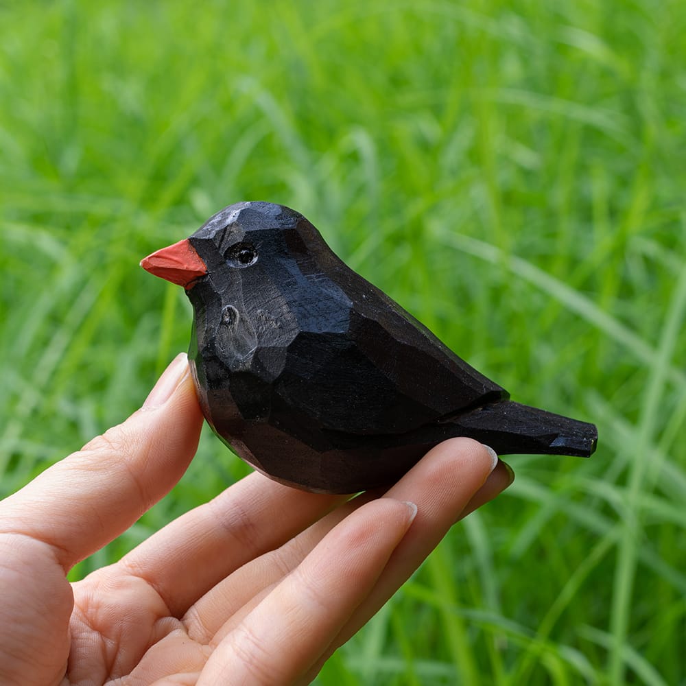 Wooden blackbird figurine held in a hand with a green grass background