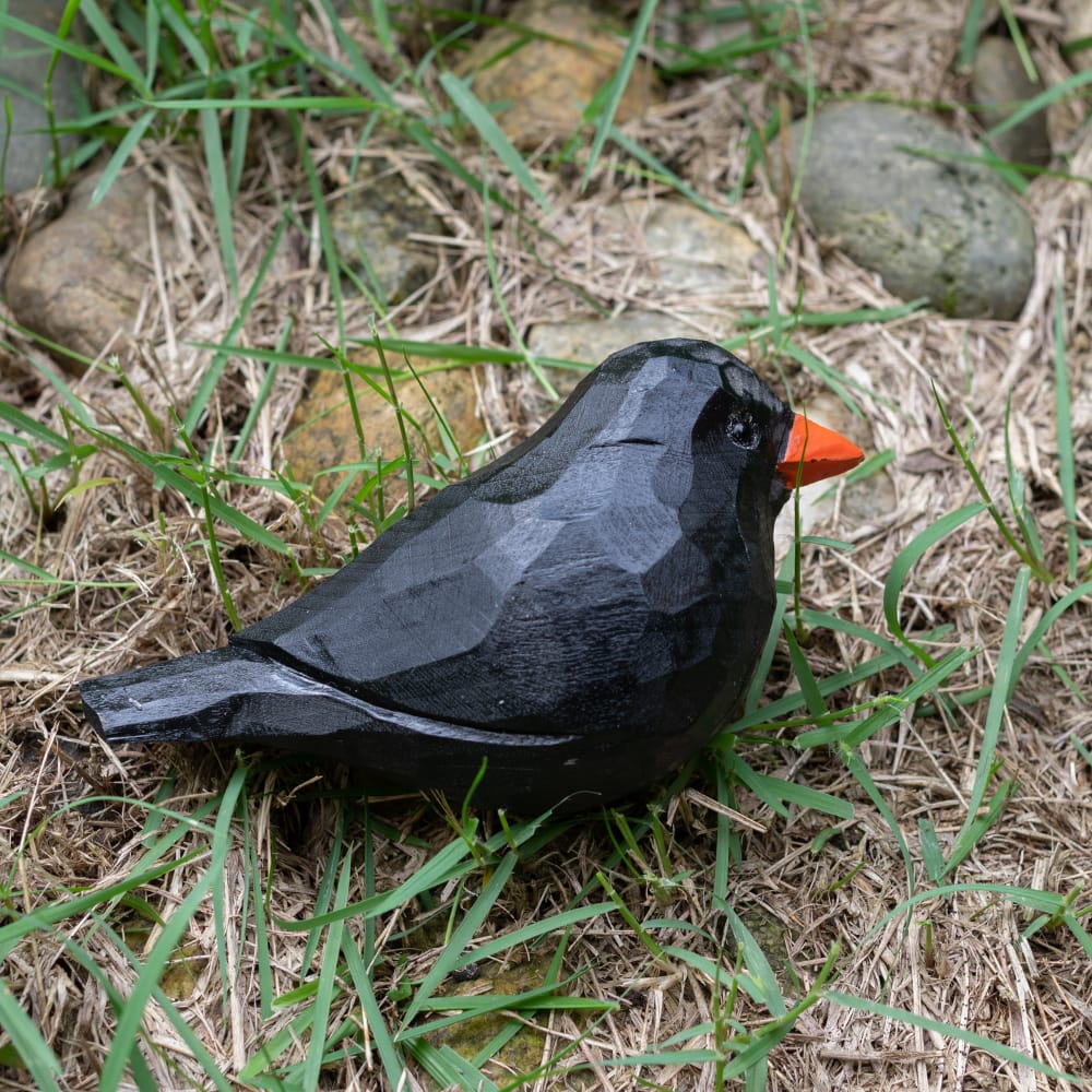 Wooden blackbird figurine with a red beak on grass and rocks