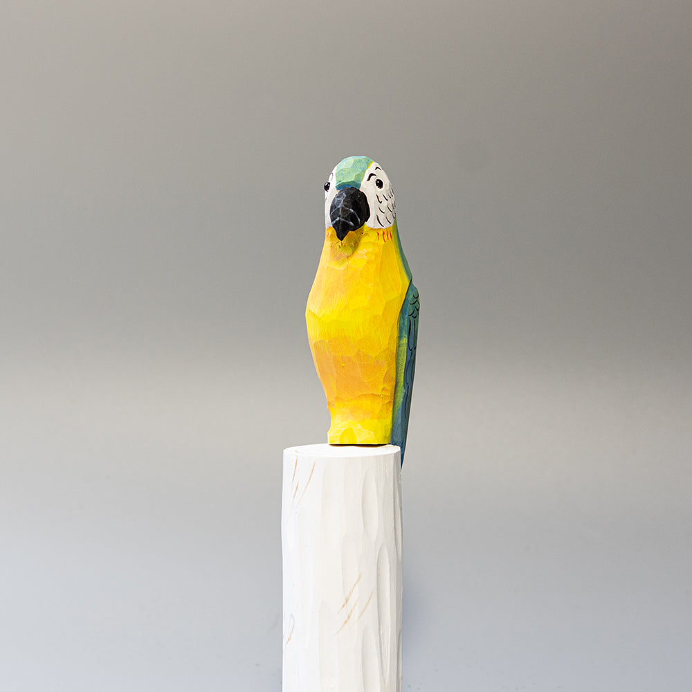 Hand-carved wooden Blue-and-yellow Macaw figurine with blue and gold plumage and white face, on a cylindrical stand. 
