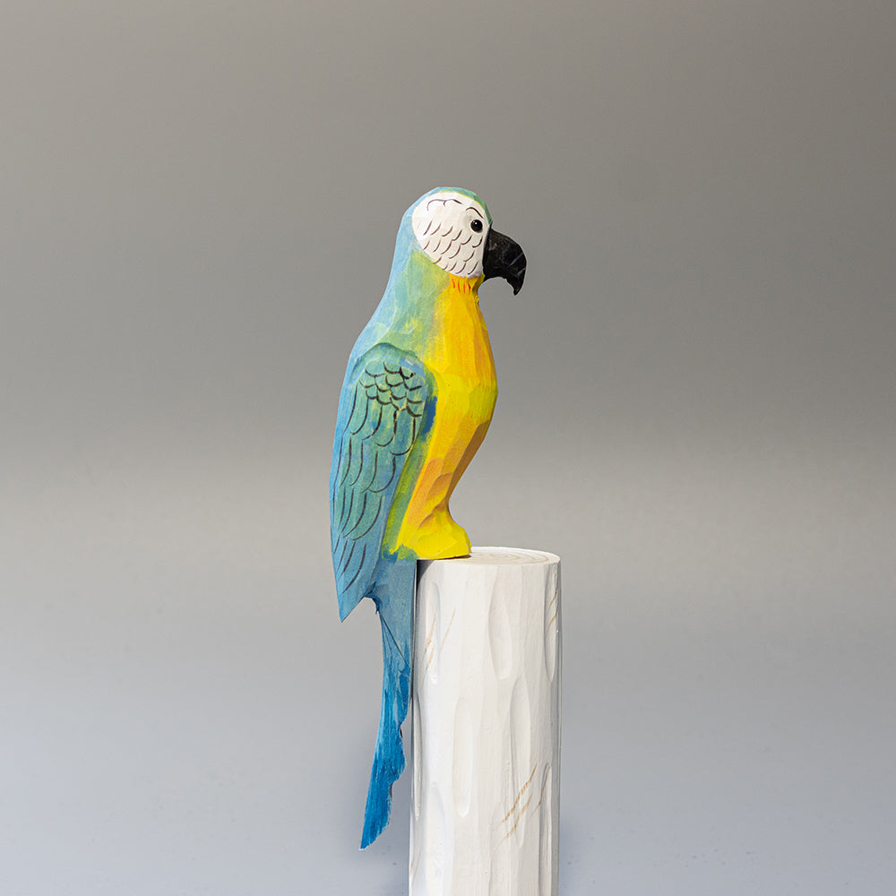 Hand-carved wooden Blue-and-yellow Macaw figurine with blue and gold plumage and white face, on a cylindrical stand. 