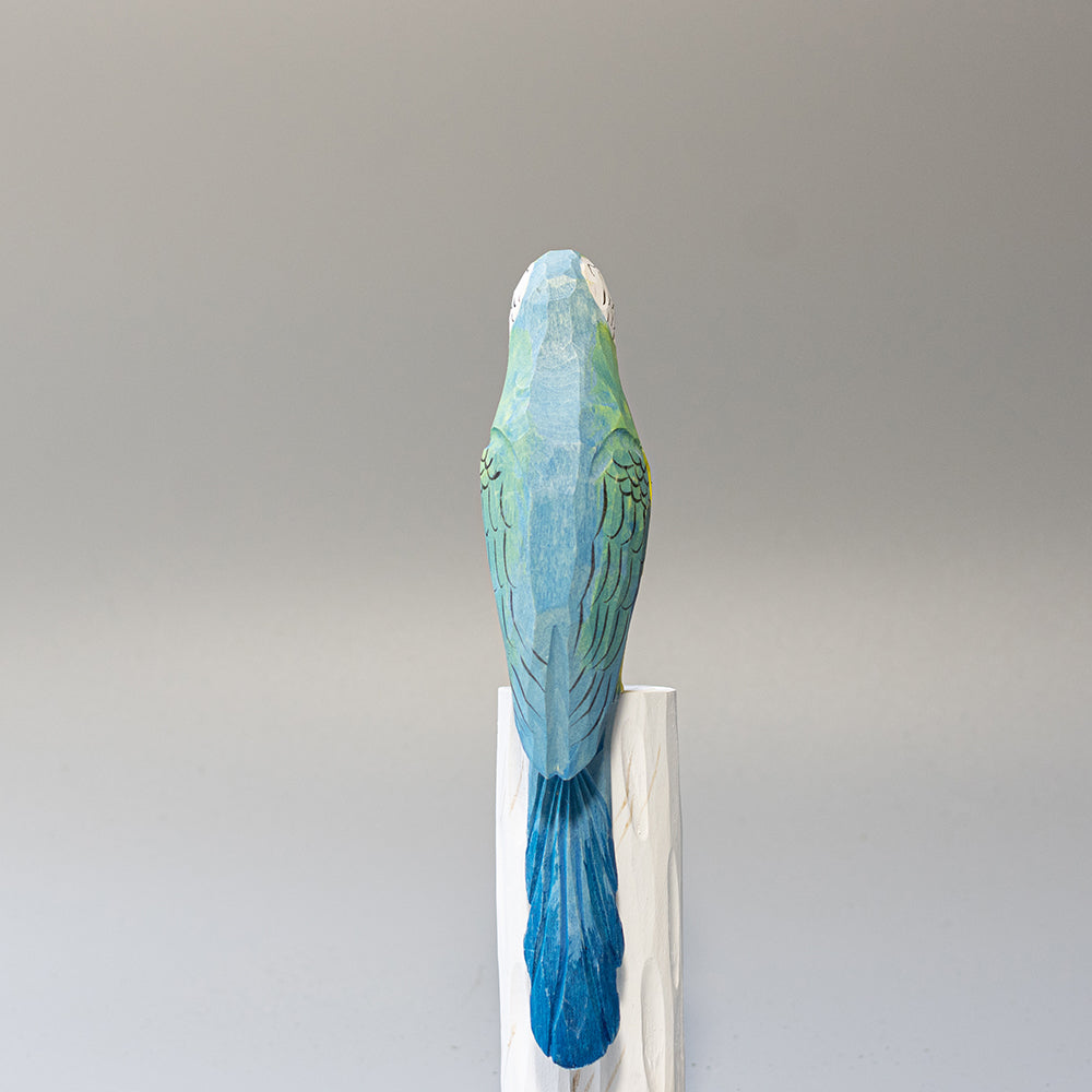 Hand-carved wooden Blue-and-yellow Macaw figurine with blue and gold plumage and white face, on a cylindrical stand. 