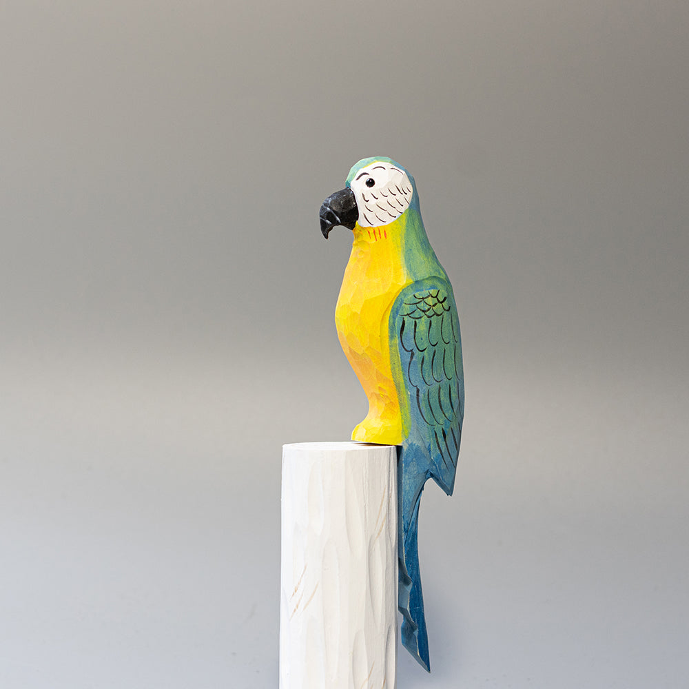 Hand-carved wooden Blue-and-yellow Macaw figurine with blue and gold plumage and white face, on a cylindrical stand. 