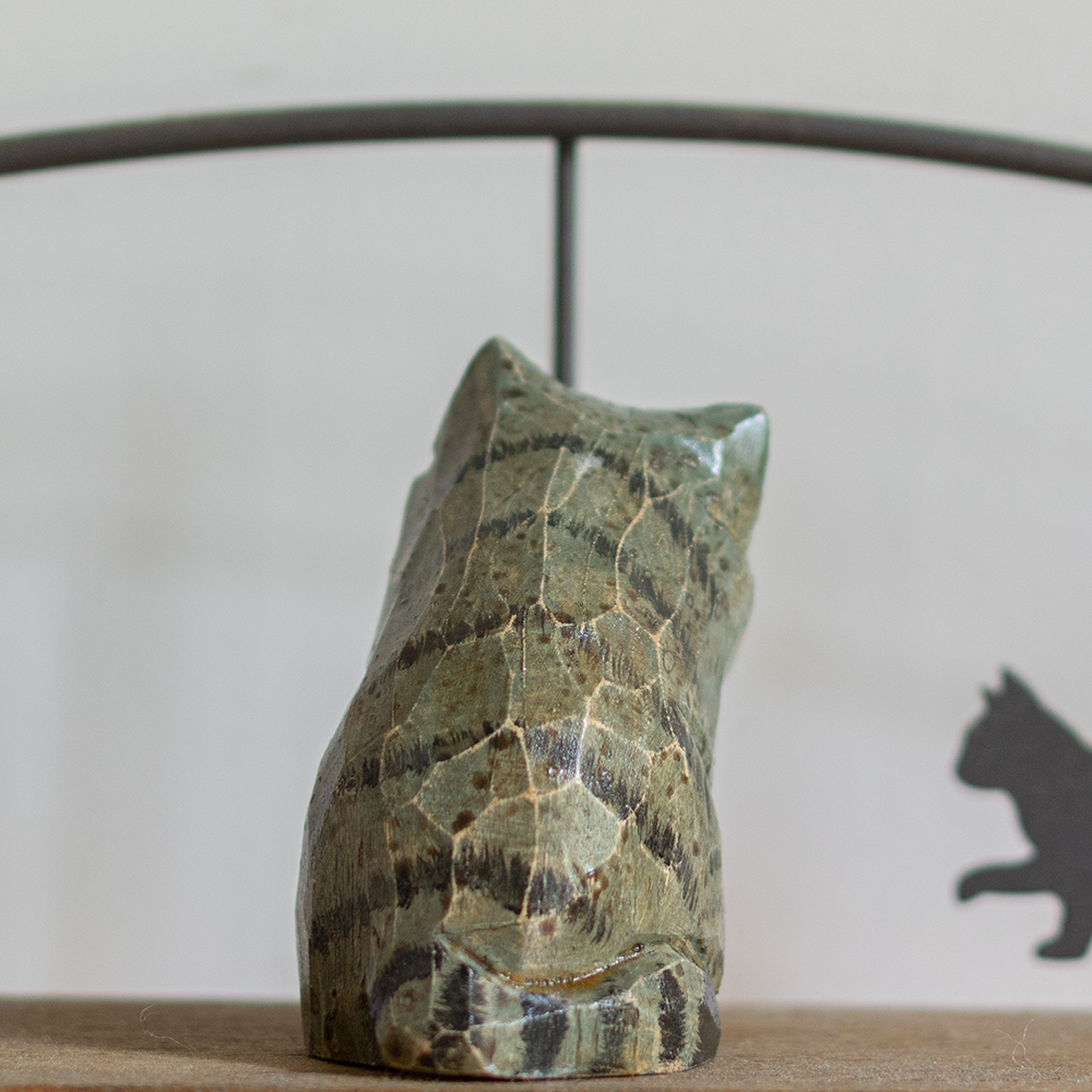 A hand-carved wooden figurine of a blue tabby cat, placed on a wooden surface.