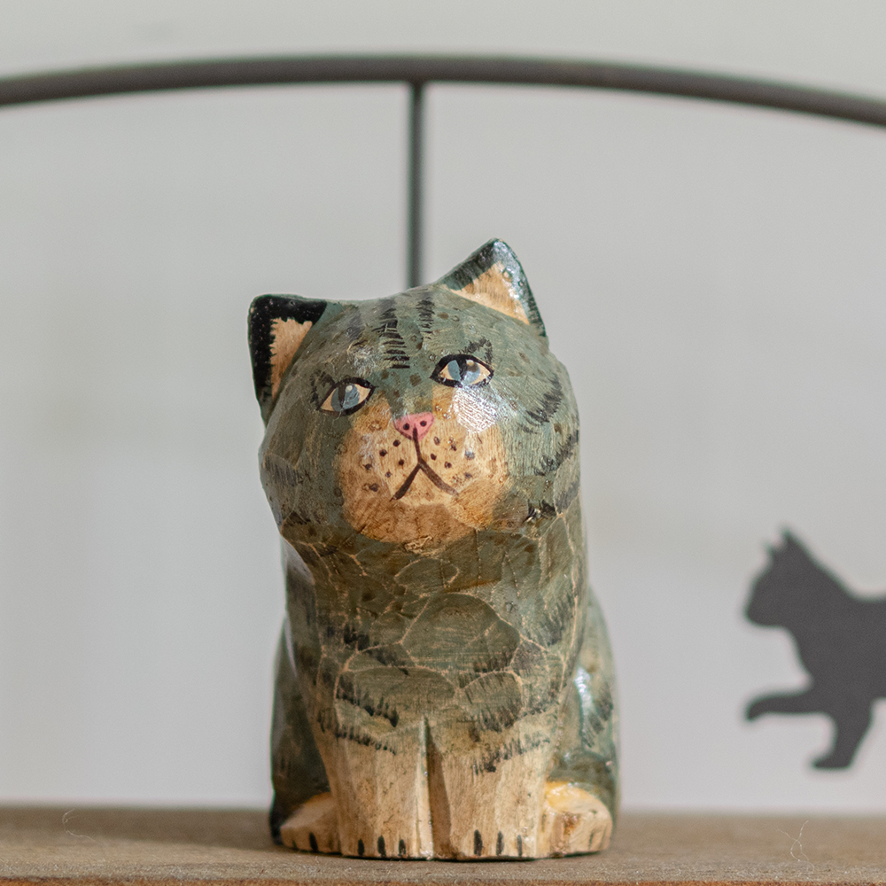 A hand-carved wooden figurine of a blue tabby cat, placed on a wooden surface.