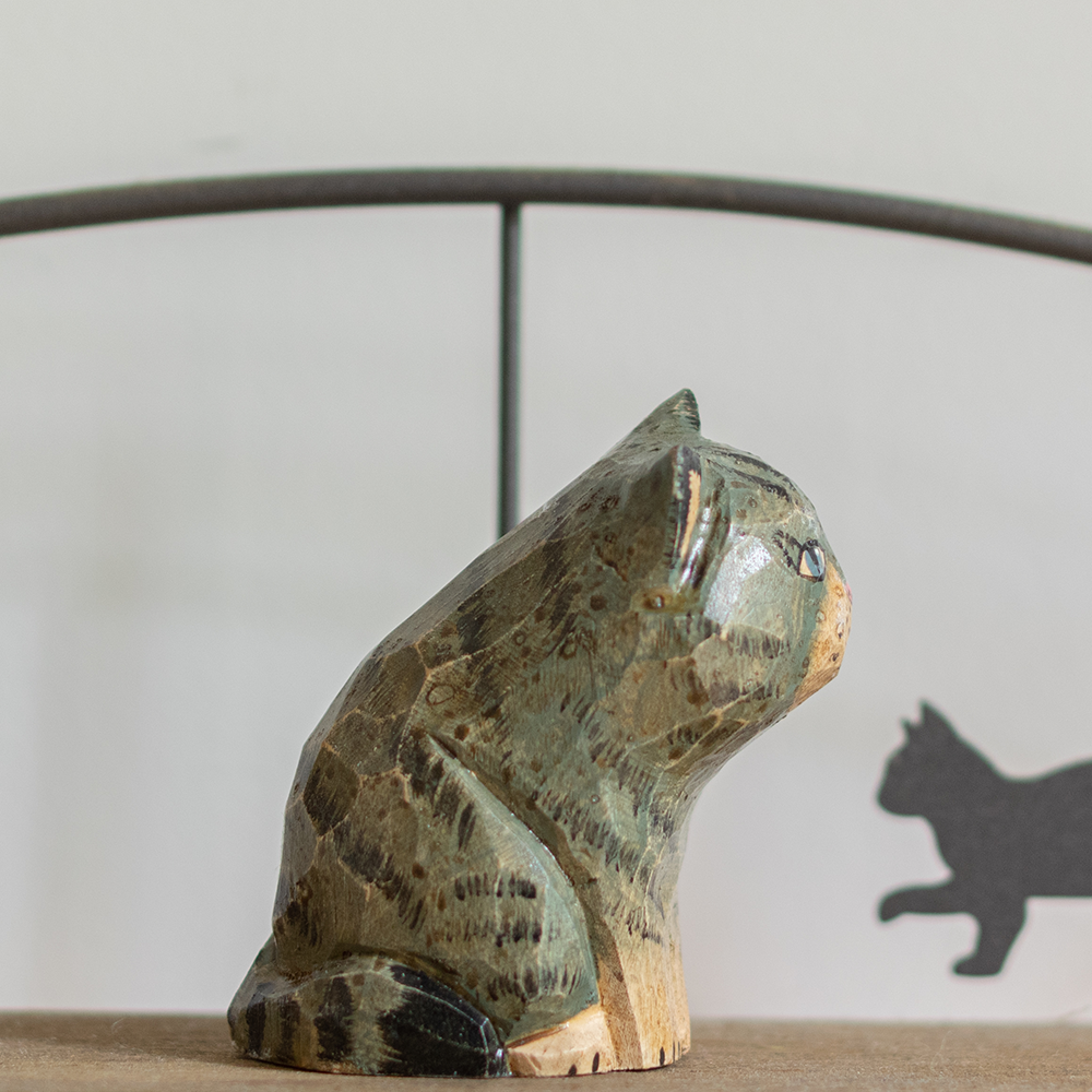 A hand-carved wooden figurine of a blue tabby cat, placed on a wooden surface.