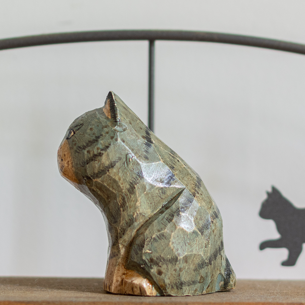 A hand-carved wooden figurine of a blue tabby cat, placed on a wooden surface.