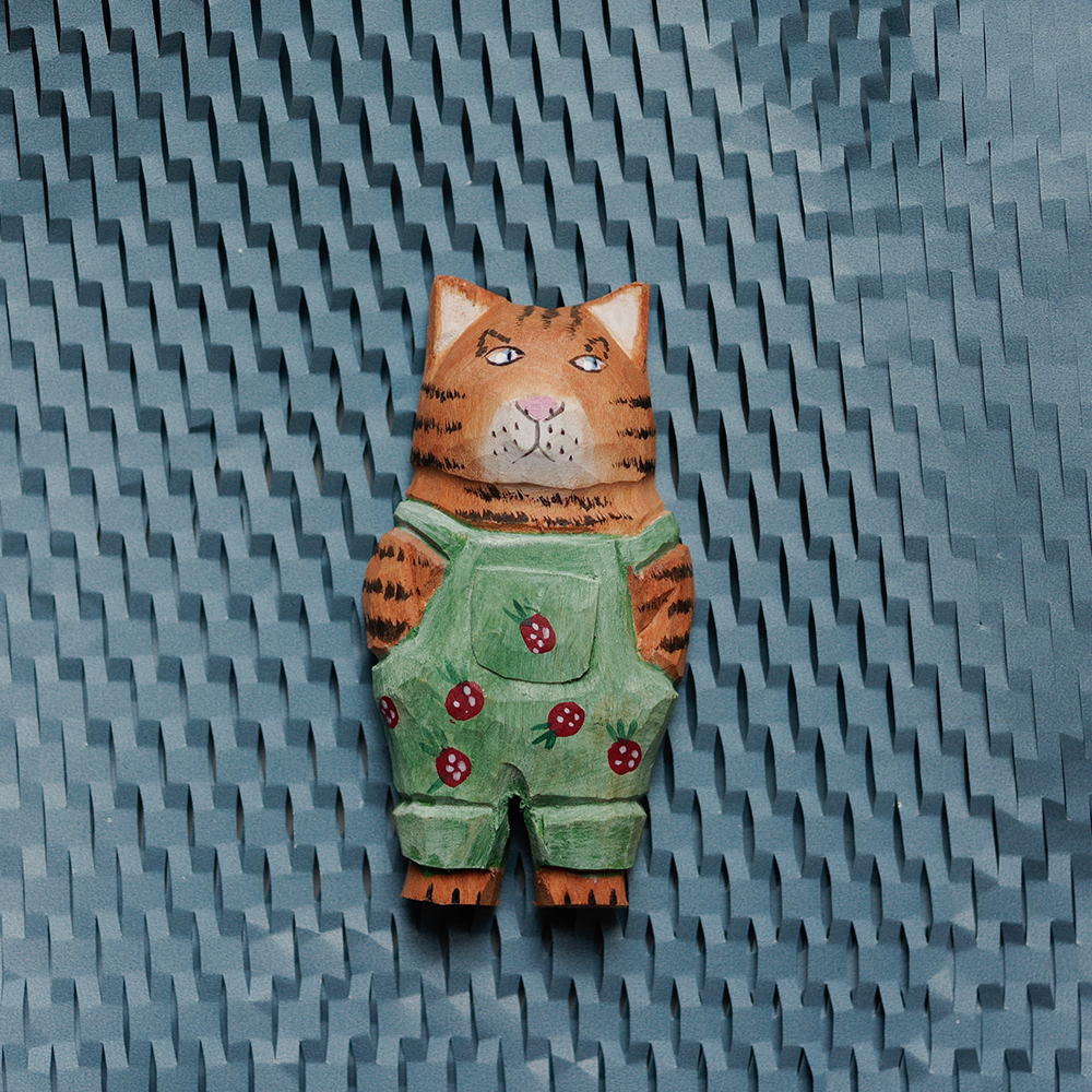 Handcrafted wooden magnet with green overalls on a textured blue background