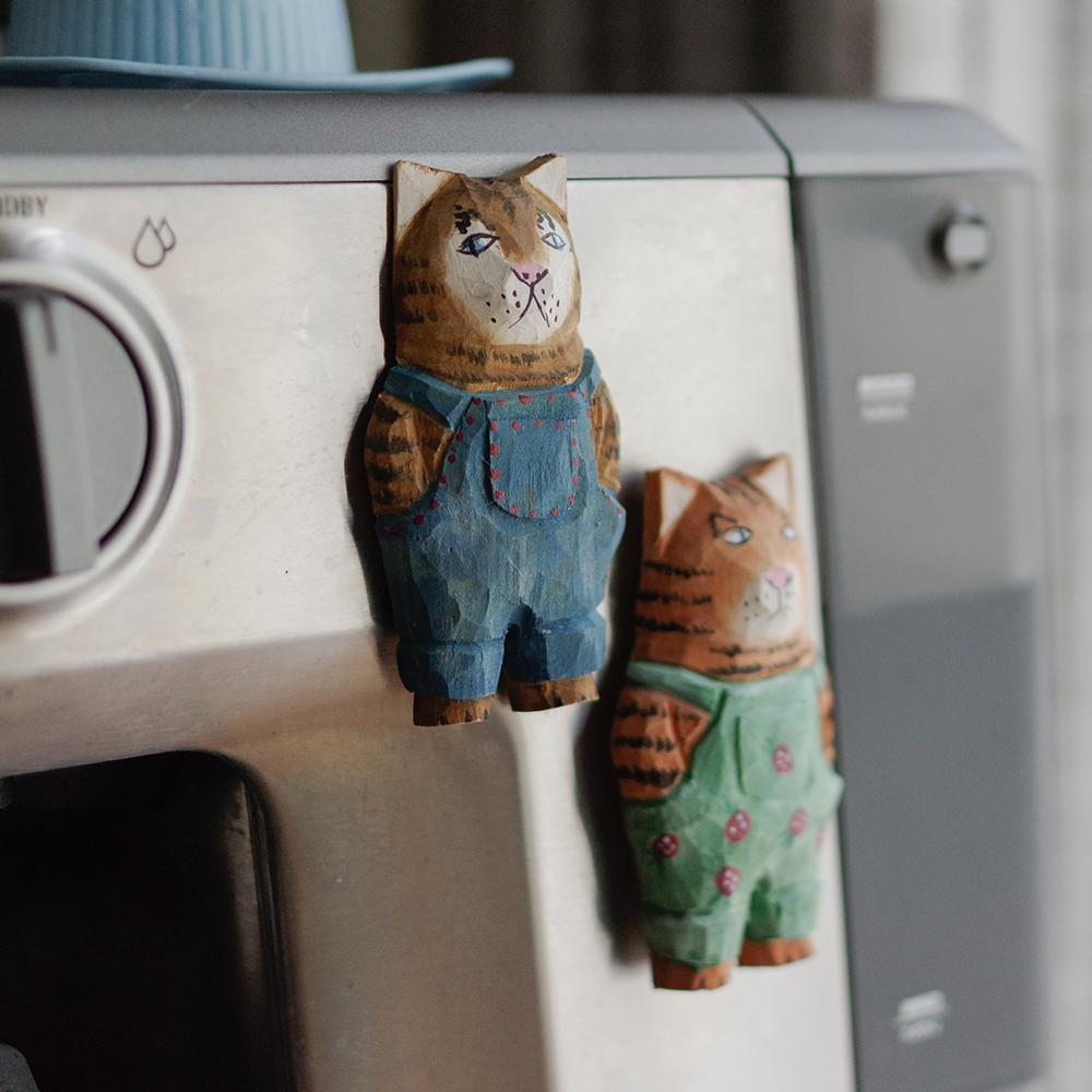 Wooden cat figurines wearing overalls attached to an espresso machine.