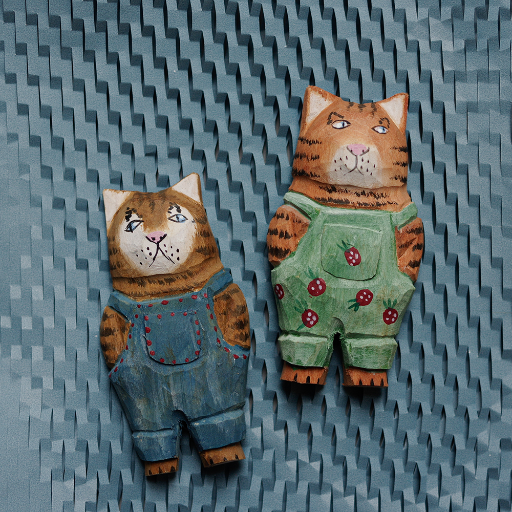 Two cat-shaped figurines wearing overalls on a textured blue background