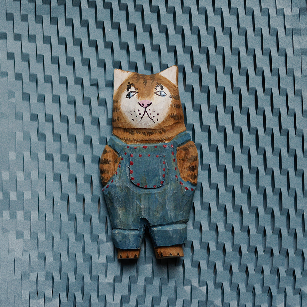handcrafted wooden cat magnet with denim overalls on a textured blue background