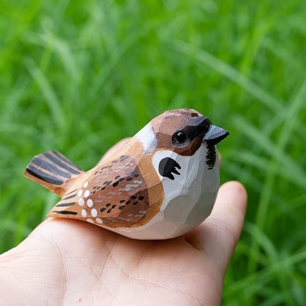 Wooden Eurasian Tree Sparrow figurine held in a hand with a blurred green grass background
