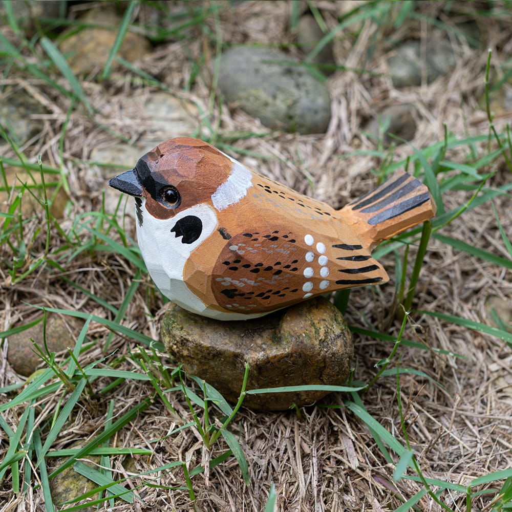 Wooden Eurasian Tree Sparrow figurine on a rock in a natural setting