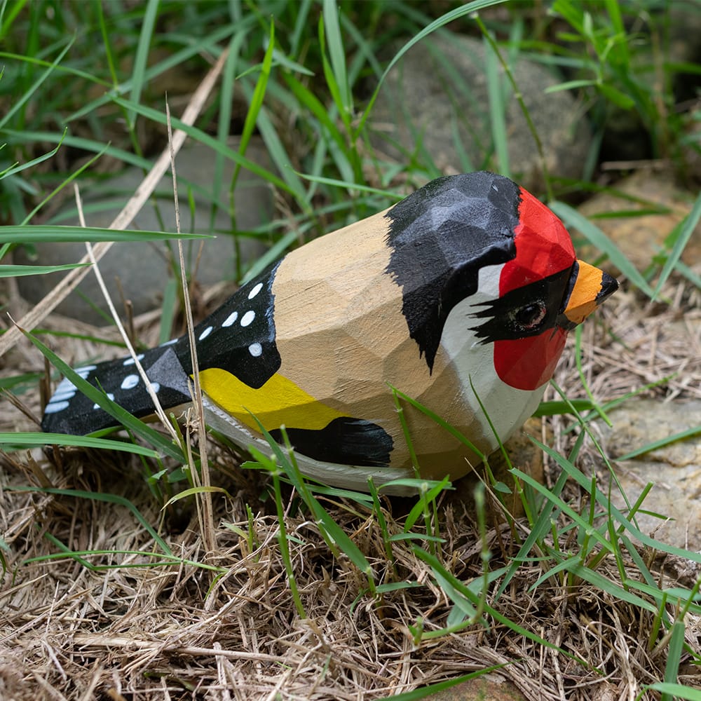 Wooden European Goldfinch figurine with colorful patterns on a grassy background