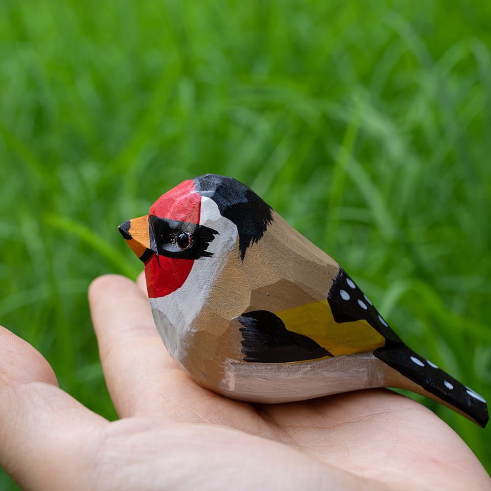 Wooden European Goldfinch figurine held in a hand with a blurred green background