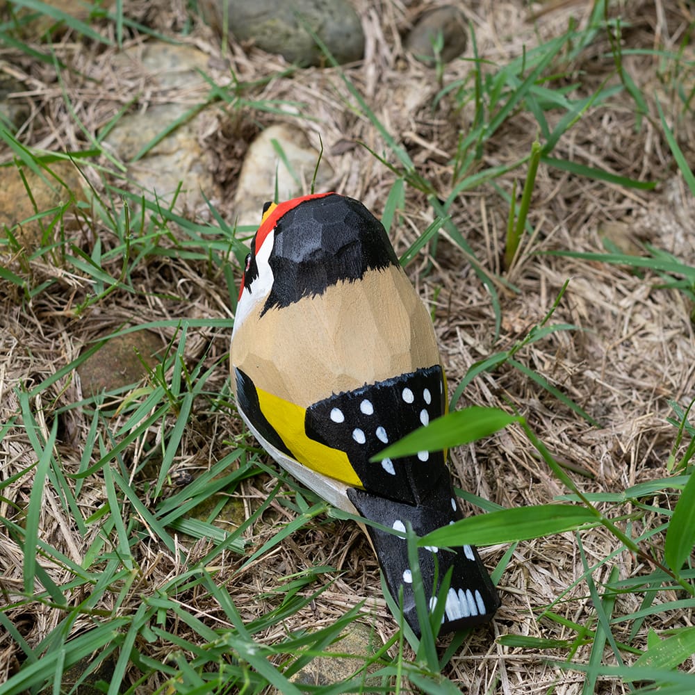 Wooden European Goldfinch figurine with colorful patterns on a grassy background