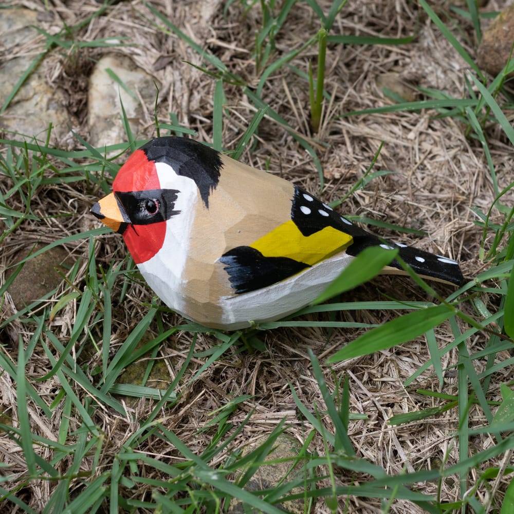 Wooden European Goldfinch figurine with colorful patterns on a grassy background
