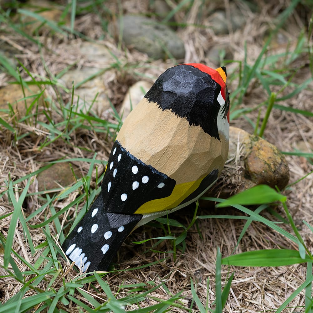 Wooden European Goldfinch figurine with colorful patterns on a grassy background