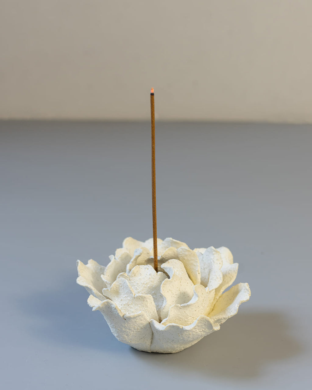 White ceramic incense holder with a single incense stick on a textured surface.