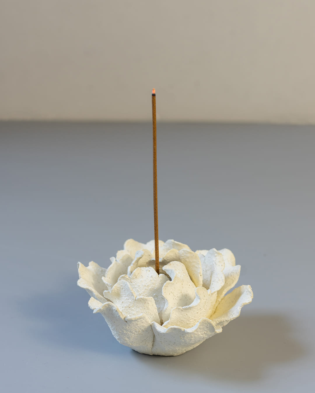 White ceramic incense holder with a single incense stick on a textured surface.