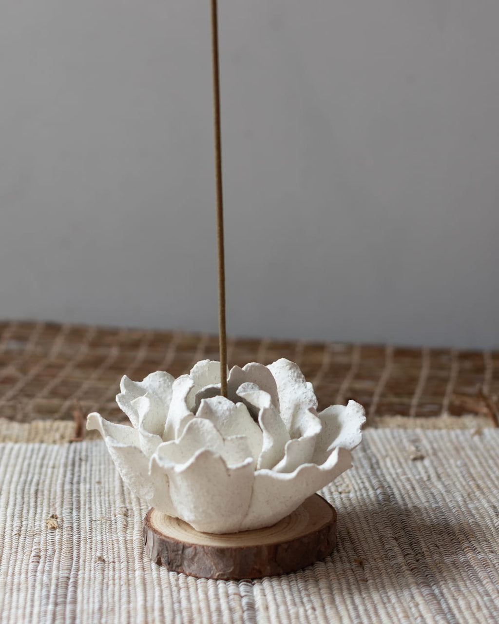 White ceramic incense holder with a single incense stick on a textured surface.