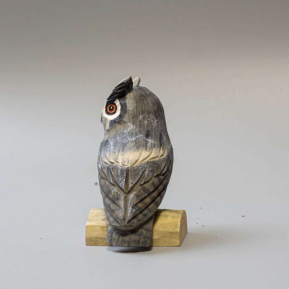 Hand carved wooden Great Horned Owl figurine showing feather tufts and mottled plumage, on a wood base. 