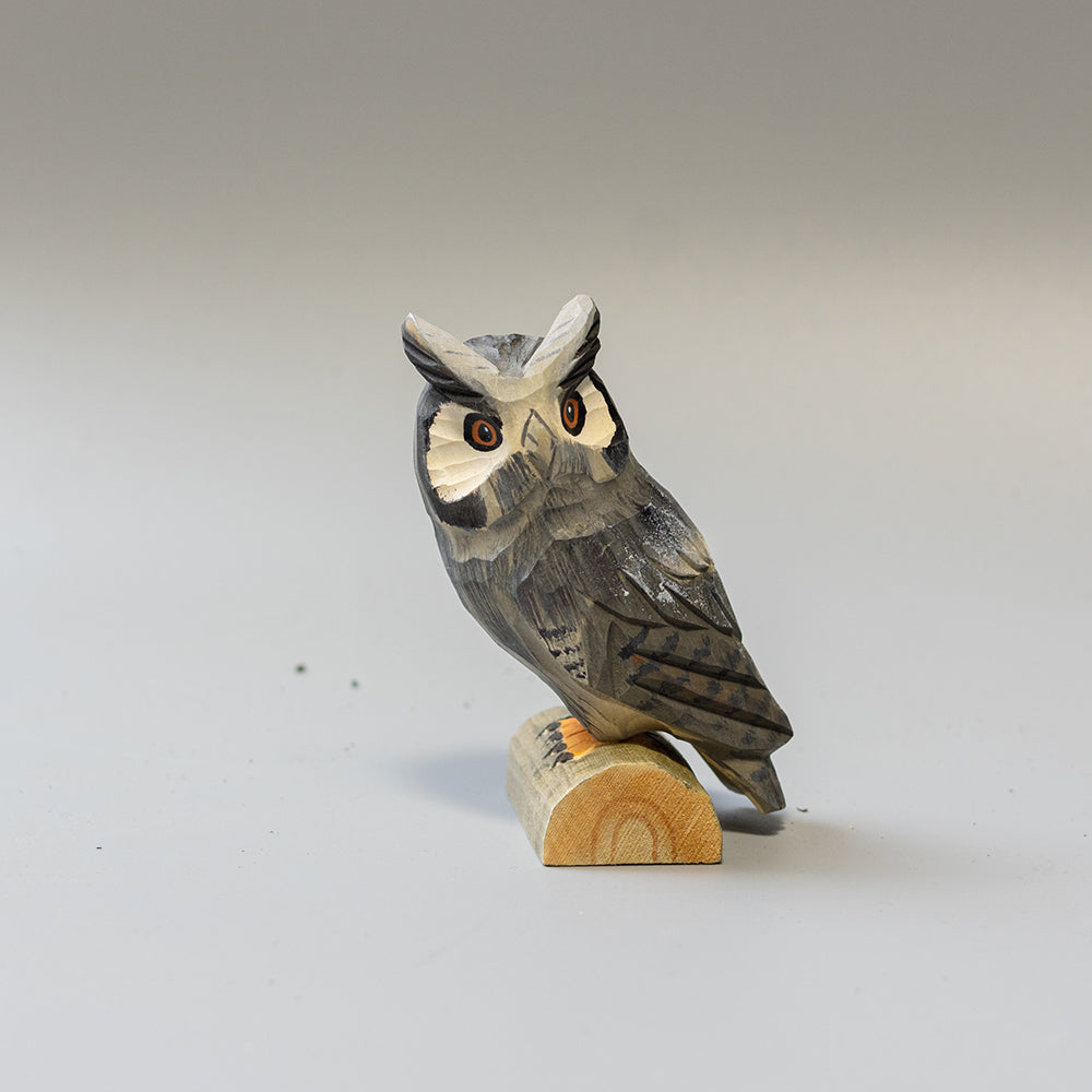 Hand carved wooden Great Horned Owl figurine showing feather tufts and mottled plumage, on a wood base. 