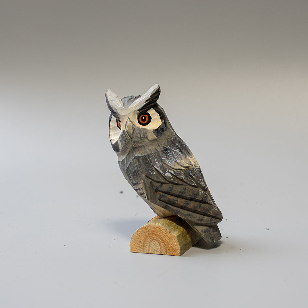Hand carved wooden Great Horned Owl figurine showing feather tufts and mottled plumage, on a wood base. 