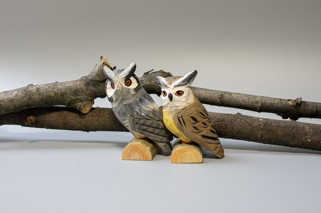 Two wooden owl figurines on a branch against a plain background