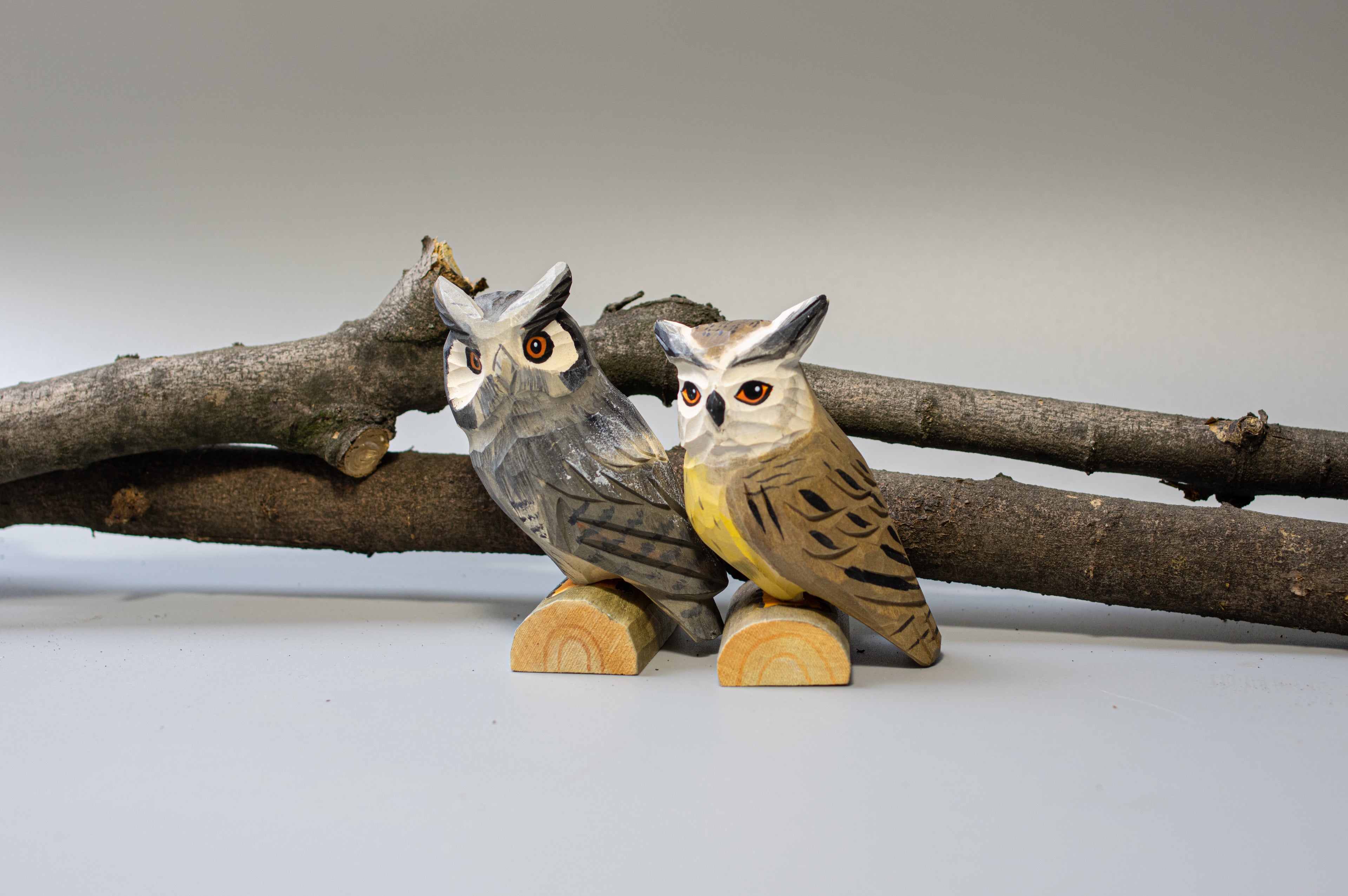 Two wooden owl figurines on a branch against a plain background