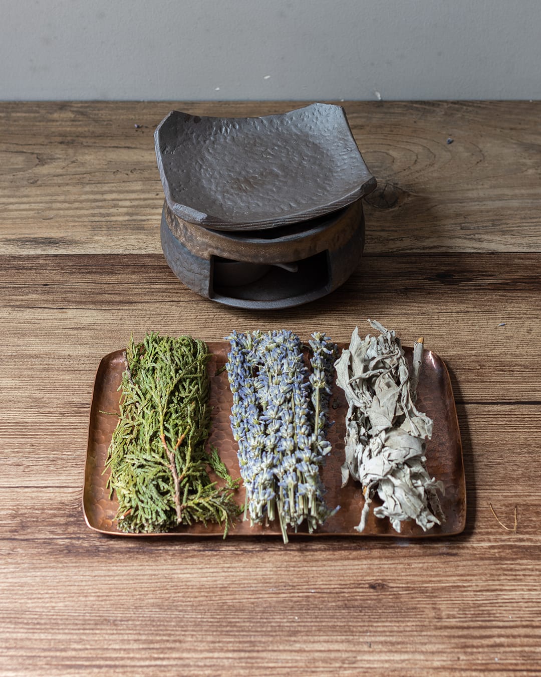 A dark, stone-textured ceramic fragrance warmer (Kawa) with a lit tealight inside, with 3 spices placing in front of it.