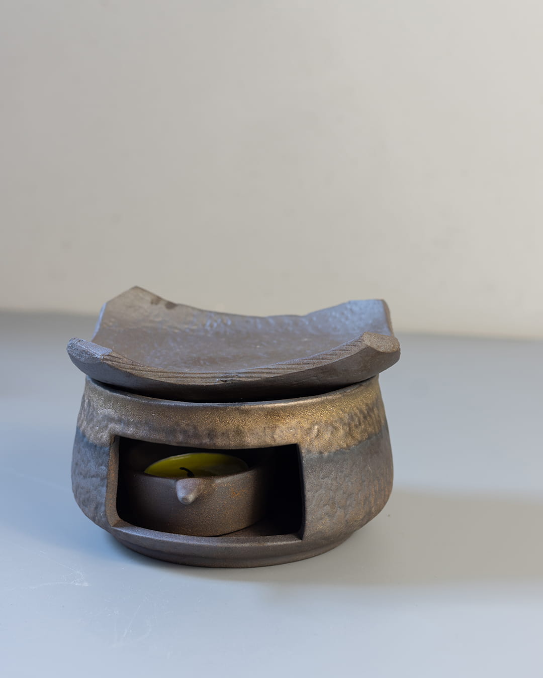 A dark, stone-textured ceramic fragrance warmer (Kawa) with a lit tealight inside, topped with a traditional Japanese-style tile.