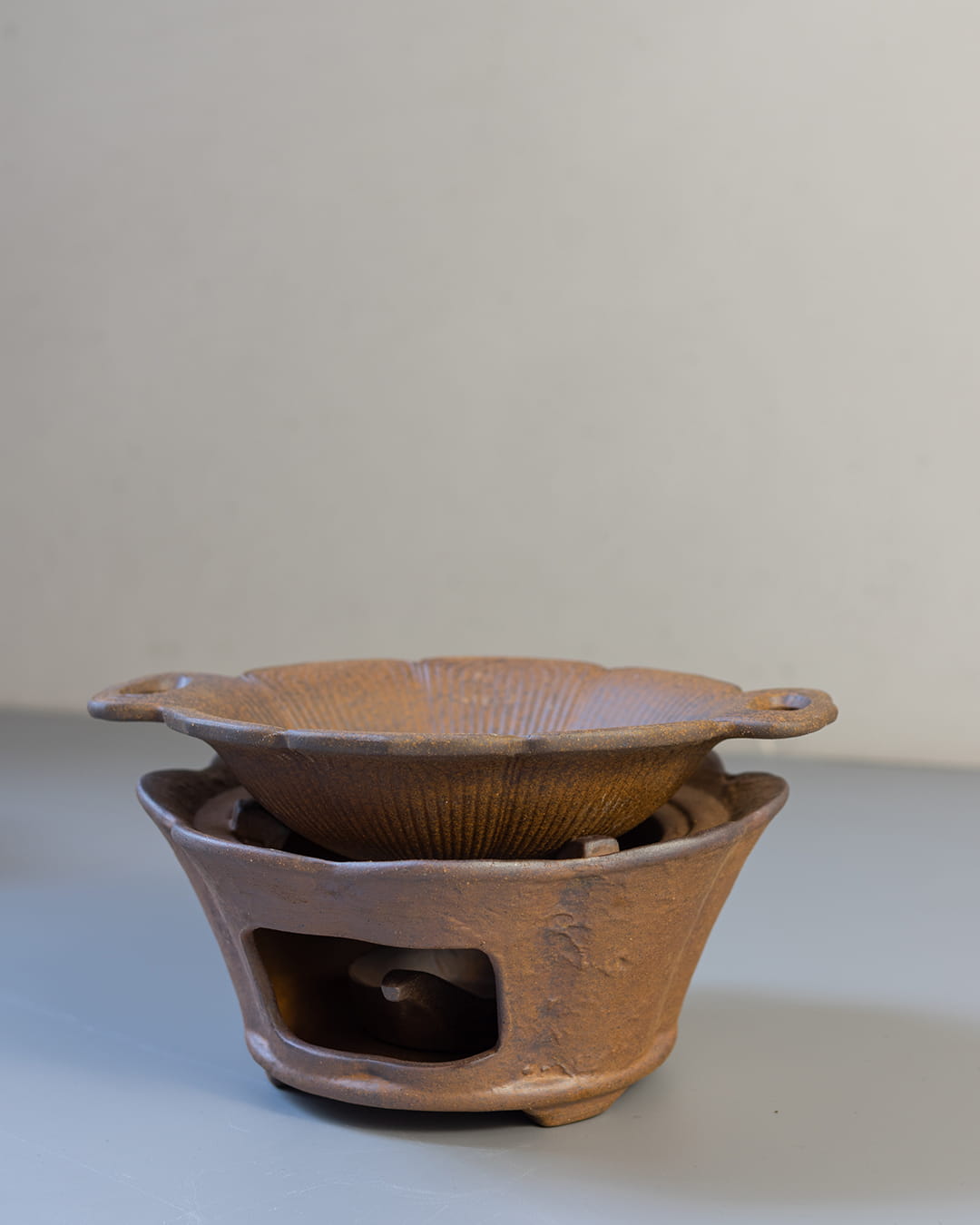 A rustic, two-piece ceramic aromatic warmer made from dark Aged Ore Clay, with a lotus-leaf-shaped dish resting on the stove base.