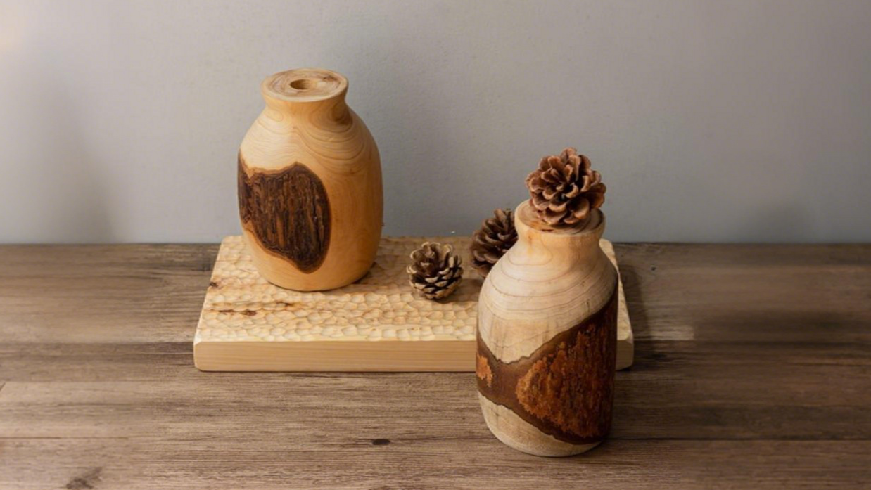 Two wooden live edge bud vases on a wooden surface with a neutral background