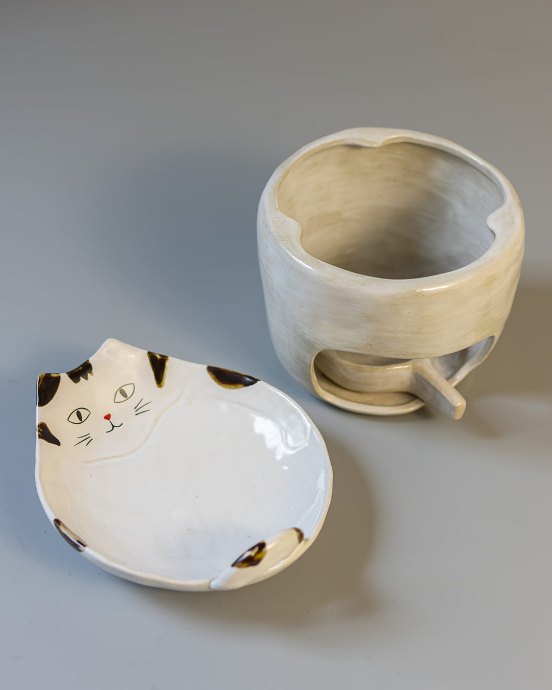 A cute, cat-shaped ceramic fragrance warmer with a white Kohiki finish, resting on its stove base with a lit tealight visible inside.