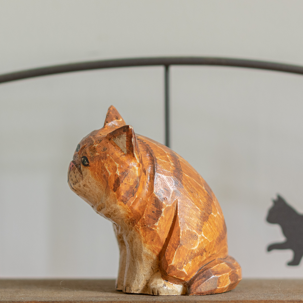 A hand-carved wooden figurine of a orange persian tabby, placed on a wooden surface.