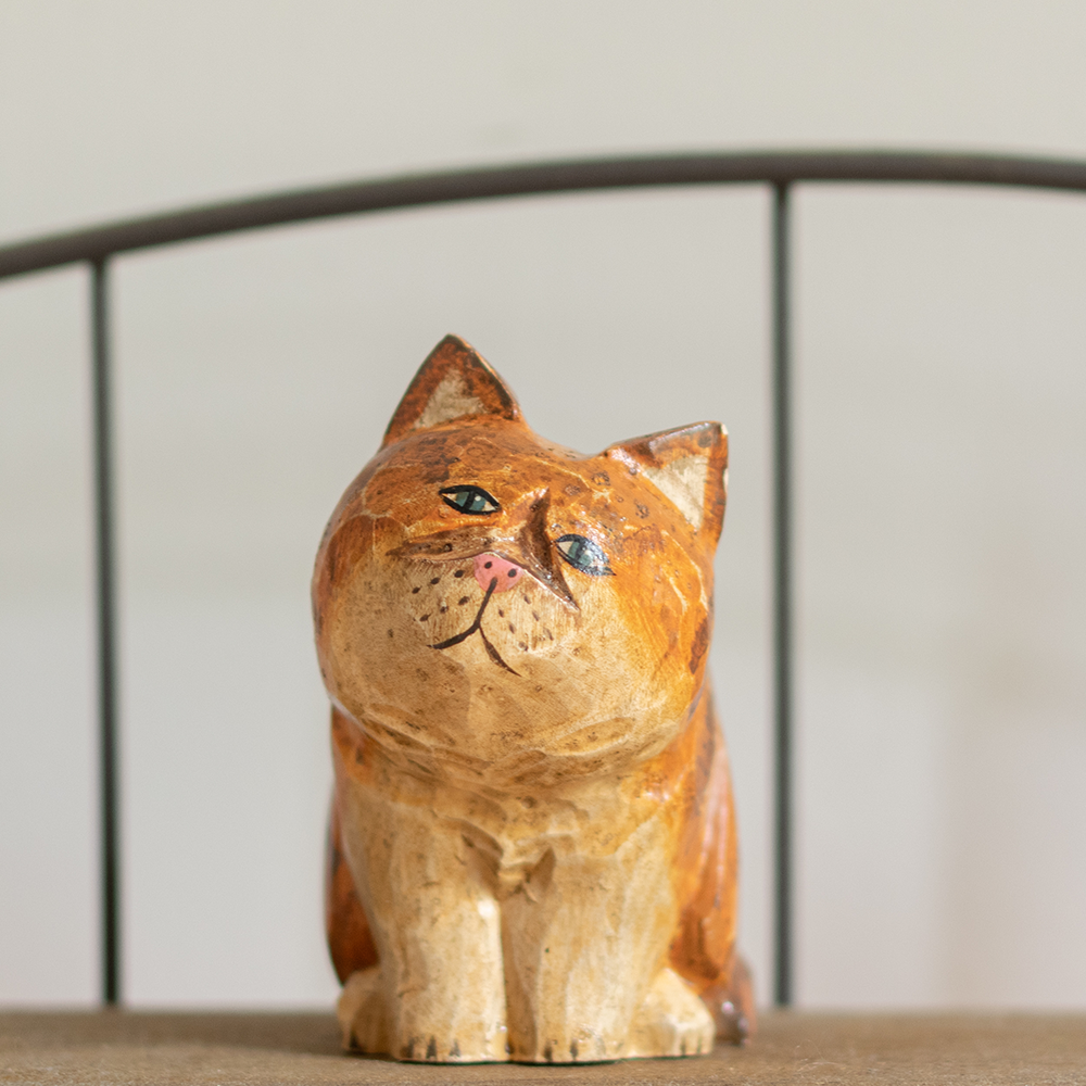 A hand-carved wooden figurine of a orange persian tabby, placed on a wooden surface.