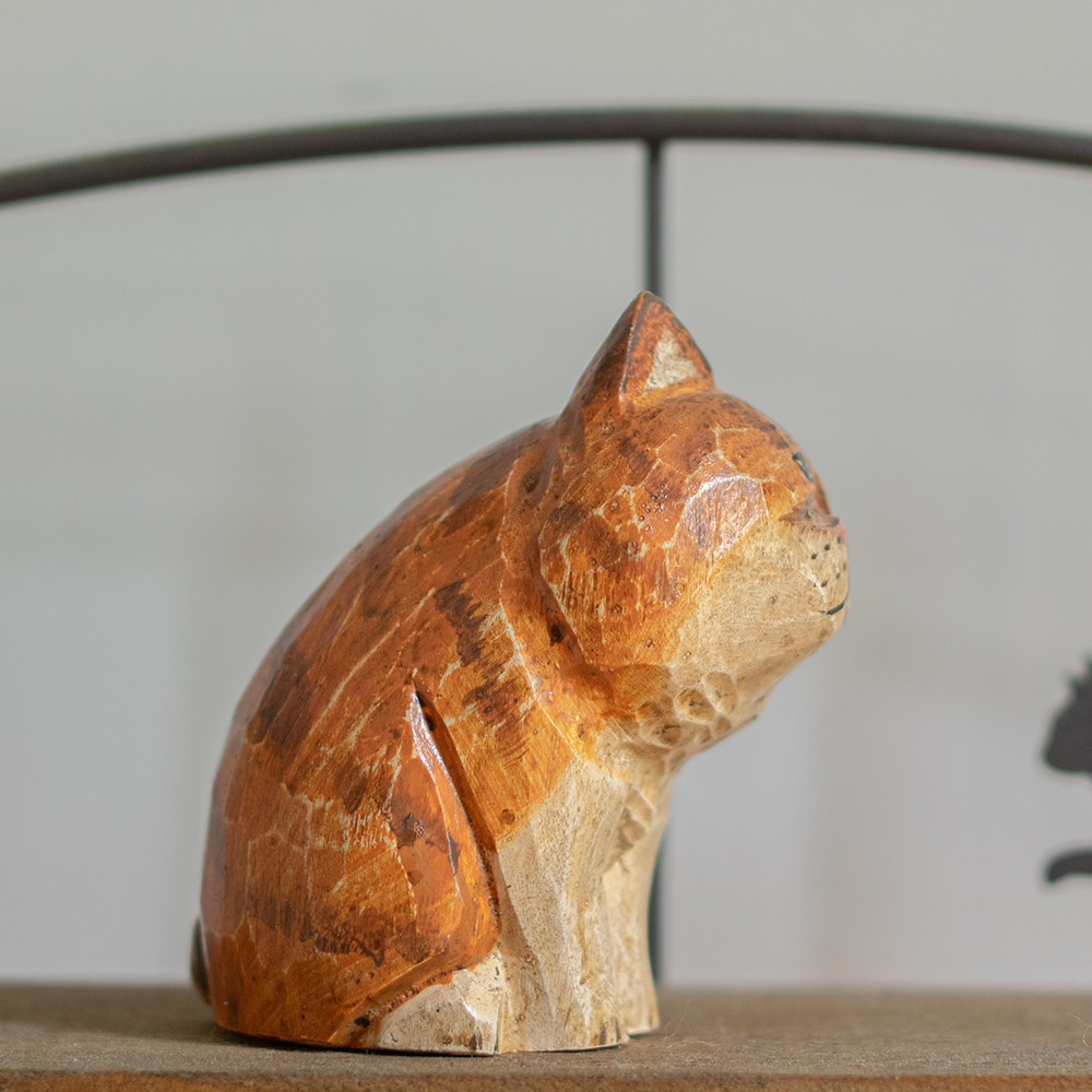 A hand-carved wooden figurine of a orange persian tabby, placed on a wooden surface.