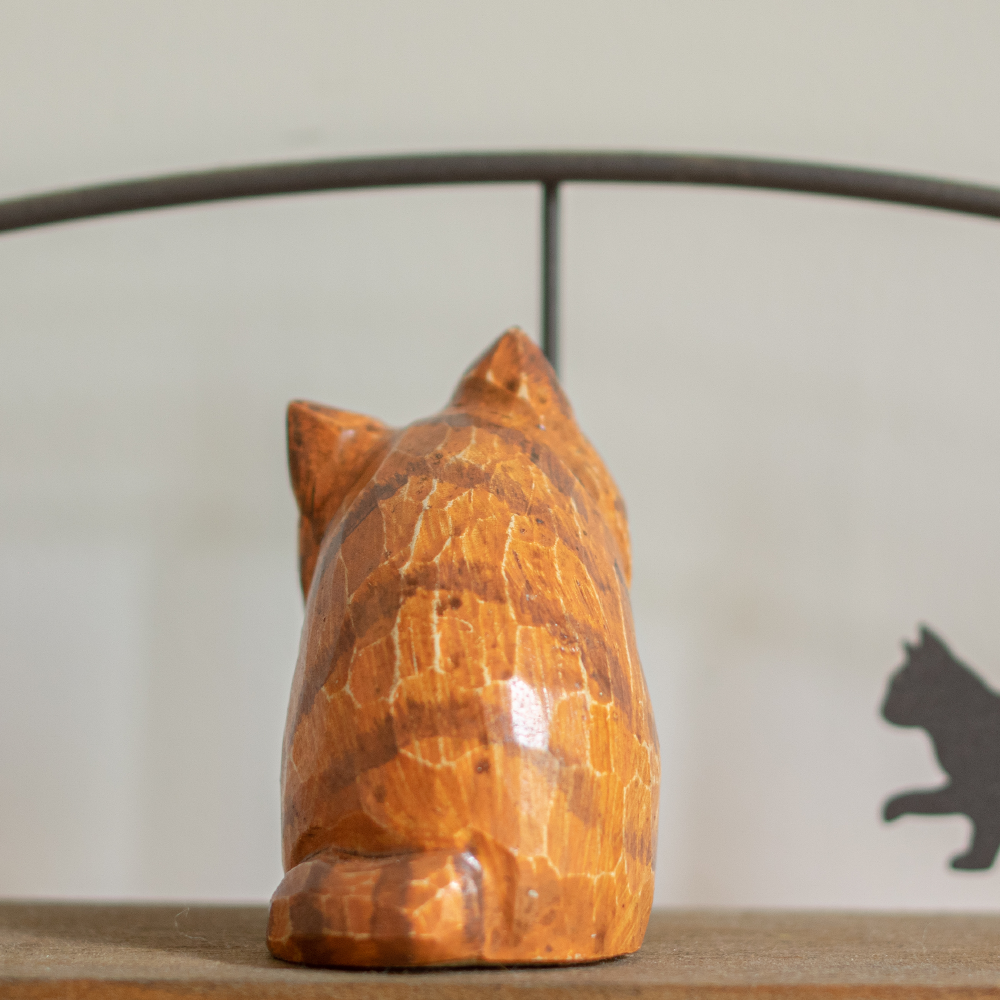A hand-carved wooden figurine of a orange persian tabby, placed on a wooden surface.