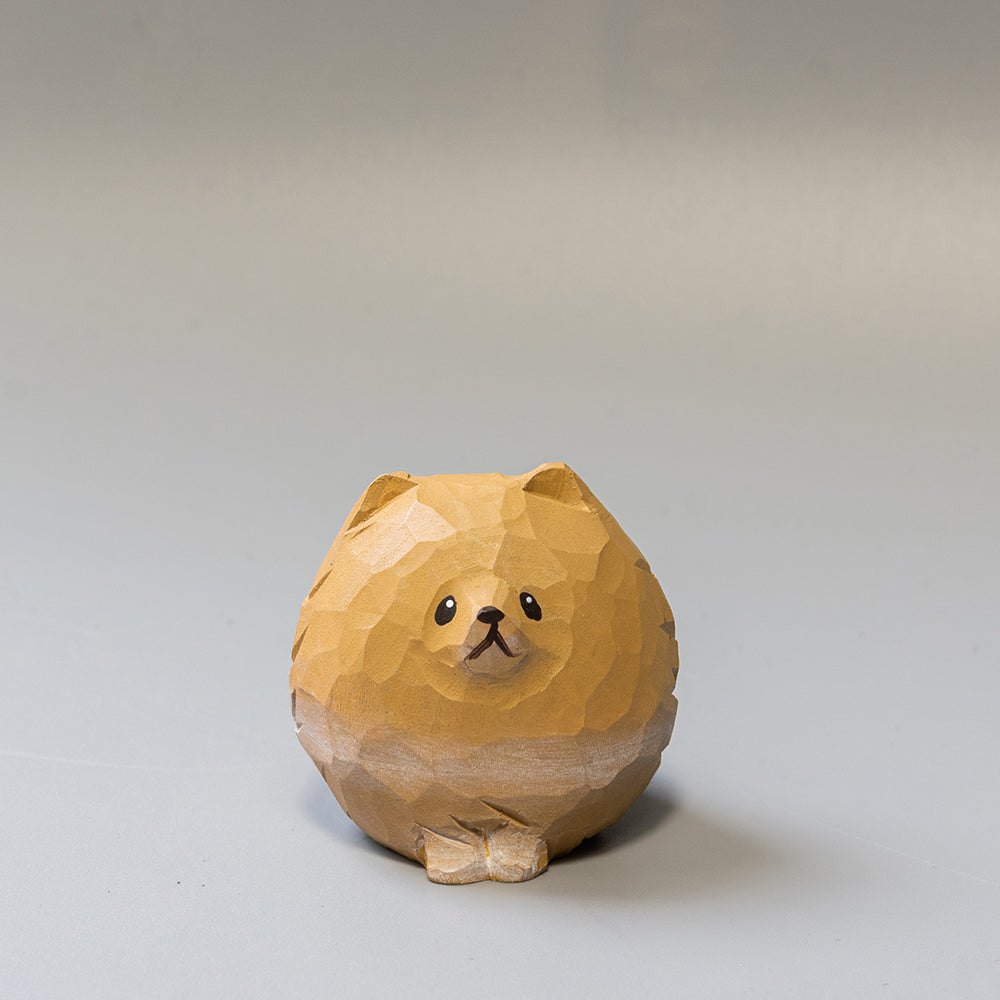 A hand-carved wooden figurine of a Pomeranian dog with a round body and plumed tail, primarily in shades of beige and brown.