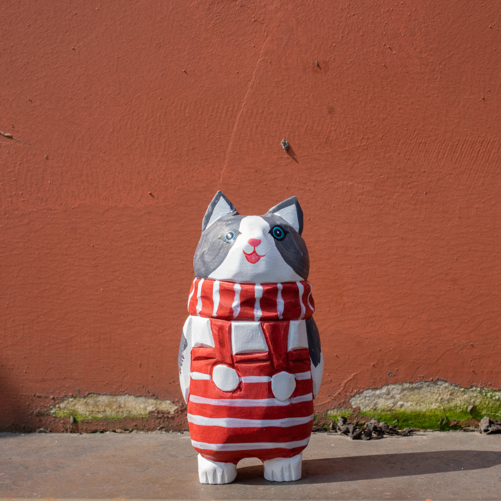 Hand-carved wooden cat figurine with a red-and-white striped scarf. Christmas-themed wood figurine, detailed wood carving, high-quality wooden figurines.