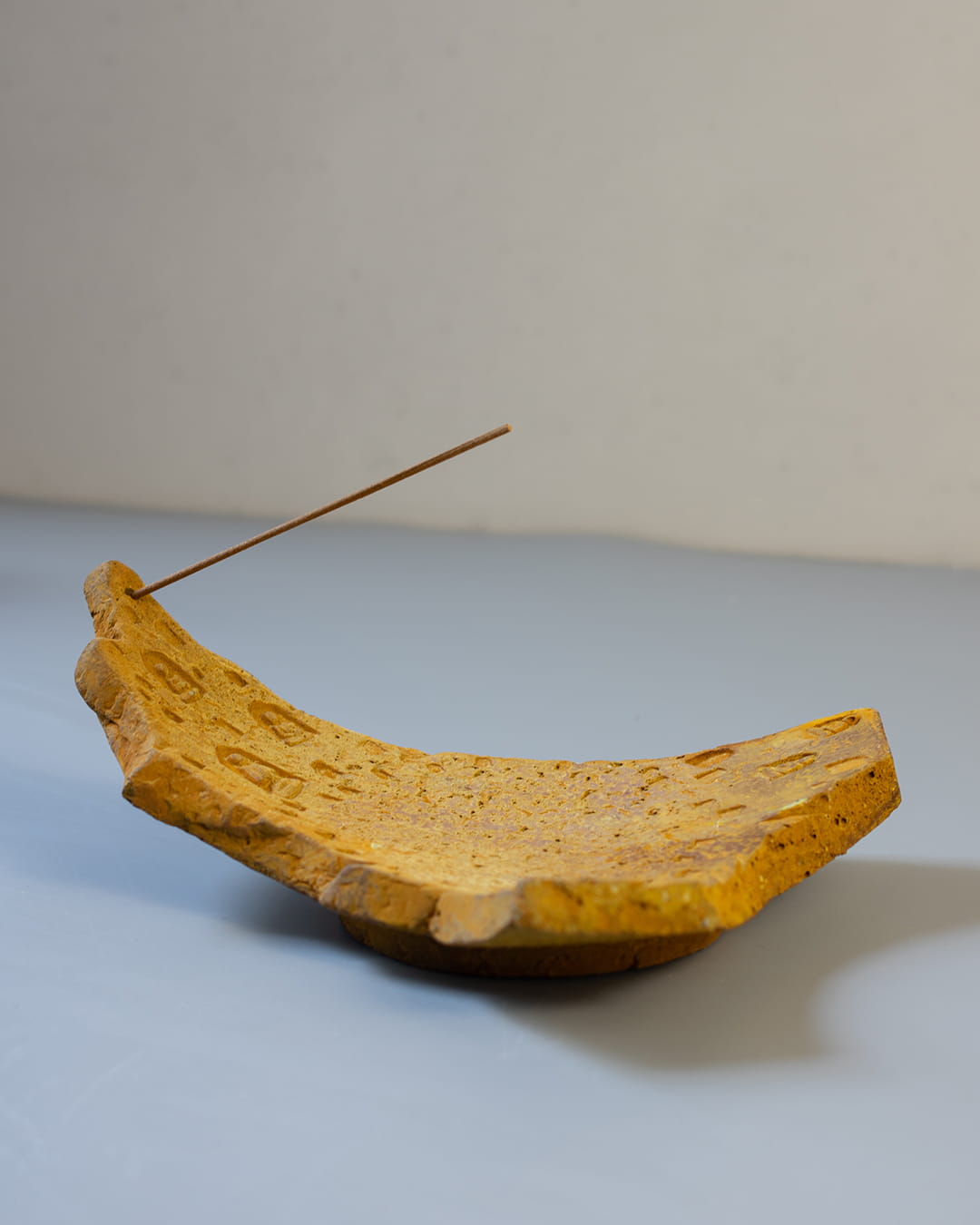 An earthy yellow cement incense plate, shaped like an ancient fragment, holding both a smoldering palo santo stick and a bundle of white sage.